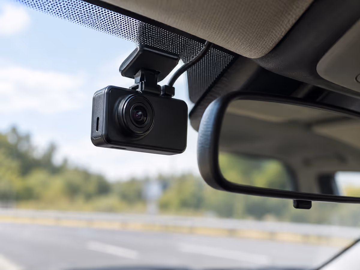 A compact dash camera is mounted inside a car.