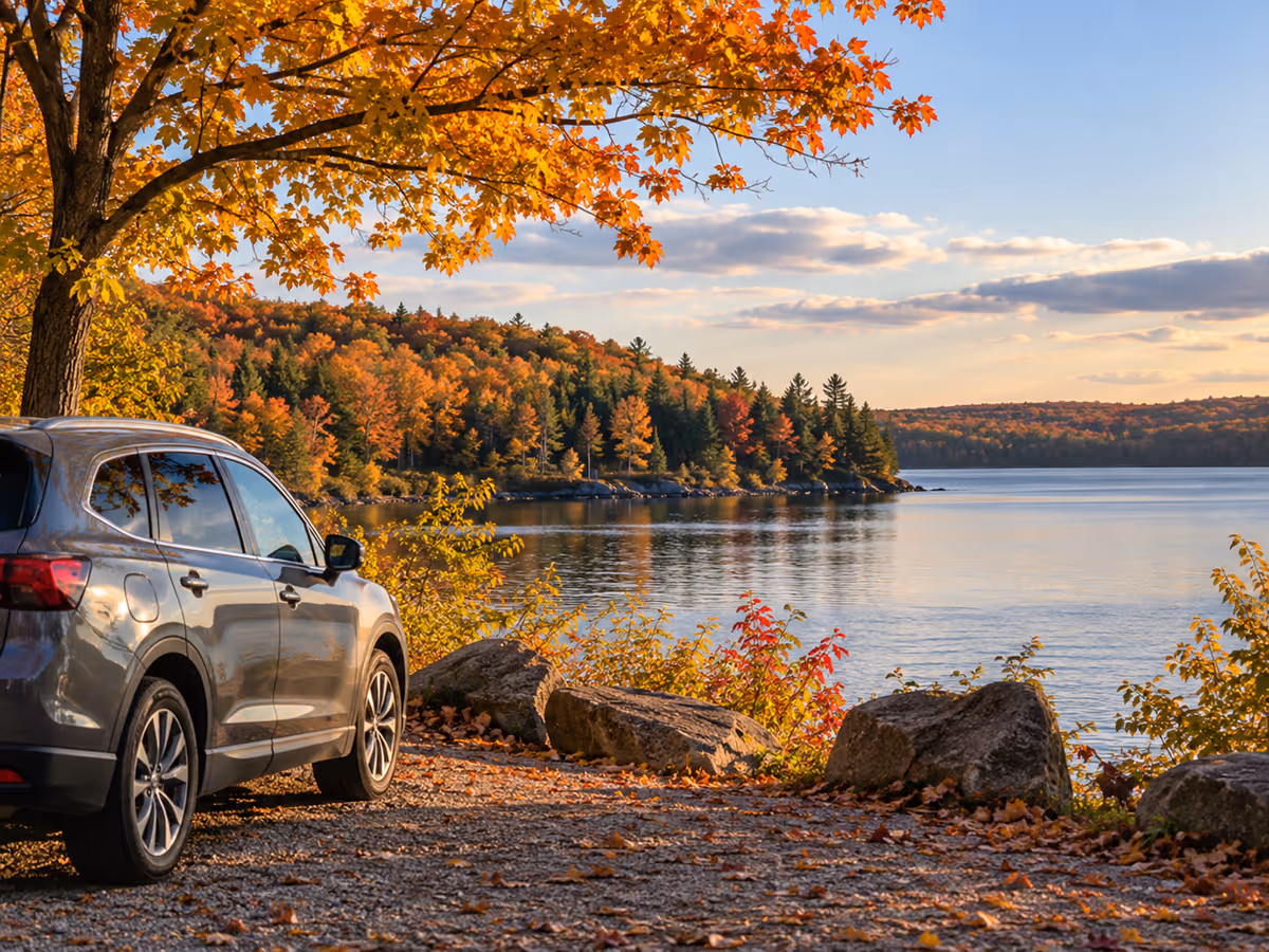 A car is parked beside a lake in autumn.